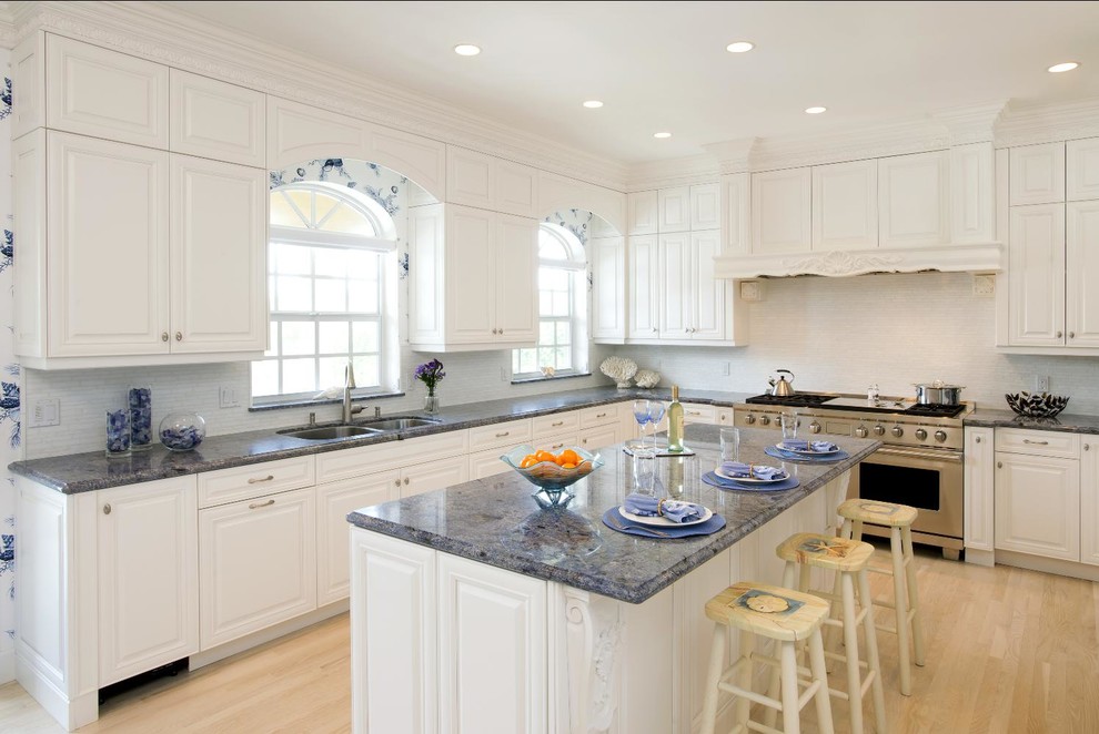 Inspiration for a mid-sized timeless u-shaped light wood floor eat-in kitchen remodel with raised-panel cabinets, an island, a double-bowl sink, white cabinets, white backsplash, glass tile backsplash, stainless steel appliances and white walls