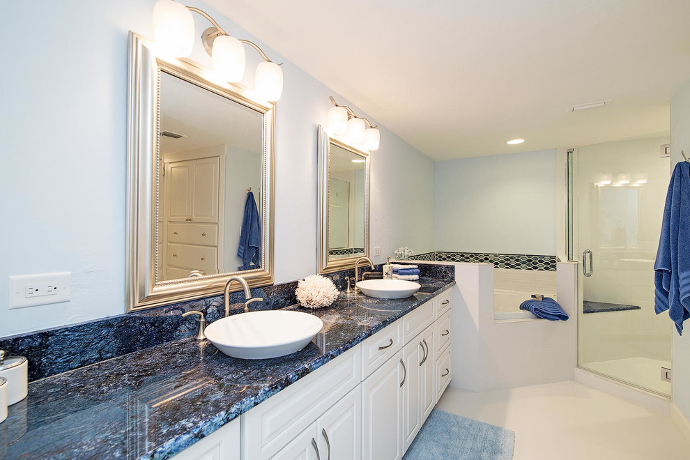 This is an example of a mid-sized traditional master bathroom in Miami with a vessel sink, recessed-panel cabinets, white cabinets, granite benchtops, a corner tub, a corner shower, white tile, porcelain tile, porcelain floors, blue walls, white floor, a hinged shower door and blue benchtops.