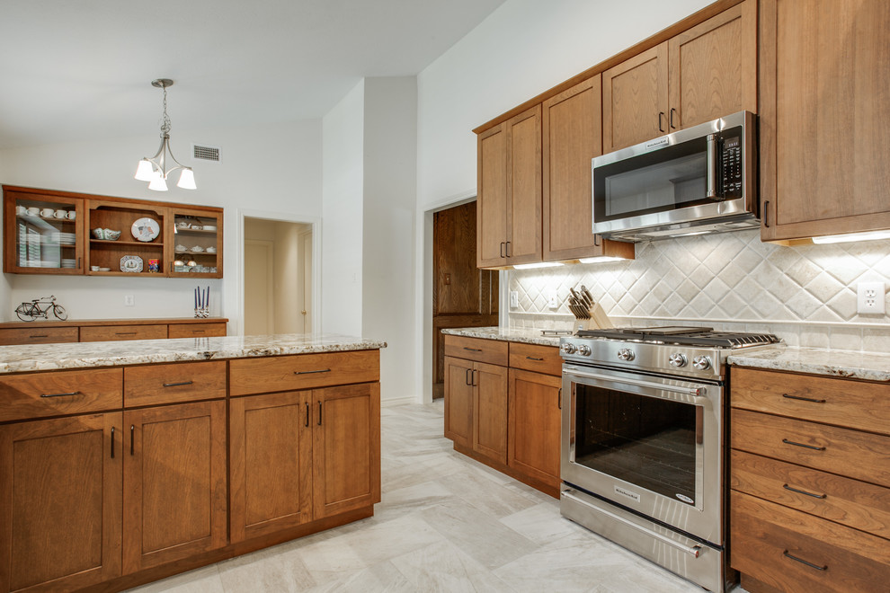 This is an example of a mid-sized arts and crafts u-shaped eat-in kitchen in Dallas with an undermount sink, shaker cabinets, medium wood cabinets, granite benchtops, beige splashback, stone tile splashback, stainless steel appliances, porcelain floors, a peninsula and beige floor.