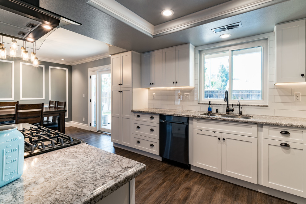 Example of a mid-sized transitional u-shaped dark wood floor and brown floor eat-in kitchen design with an undermount sink, shaker cabinets, white cabinets, granite countertops, white backsplash, subway tile backsplash, stainless steel appliances and an island