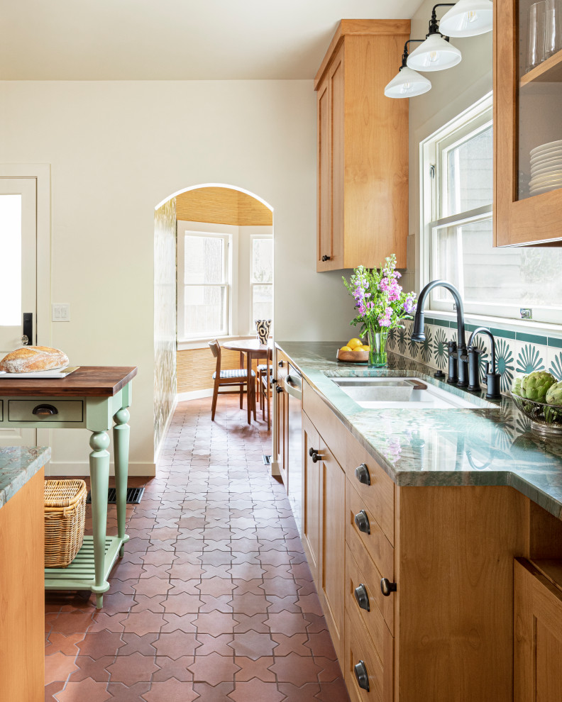 Inredning av ett eklektiskt avskilt, mellanstort grön grönt l-kök, med en undermonterad diskho, skåp i shakerstil, skåp i mellenmörkt trä, bänkskiva i kvartsit, grönt stänkskydd, stänkskydd i terrakottakakel, rostfria vitvaror, klinkergolv i porslin och orange golv