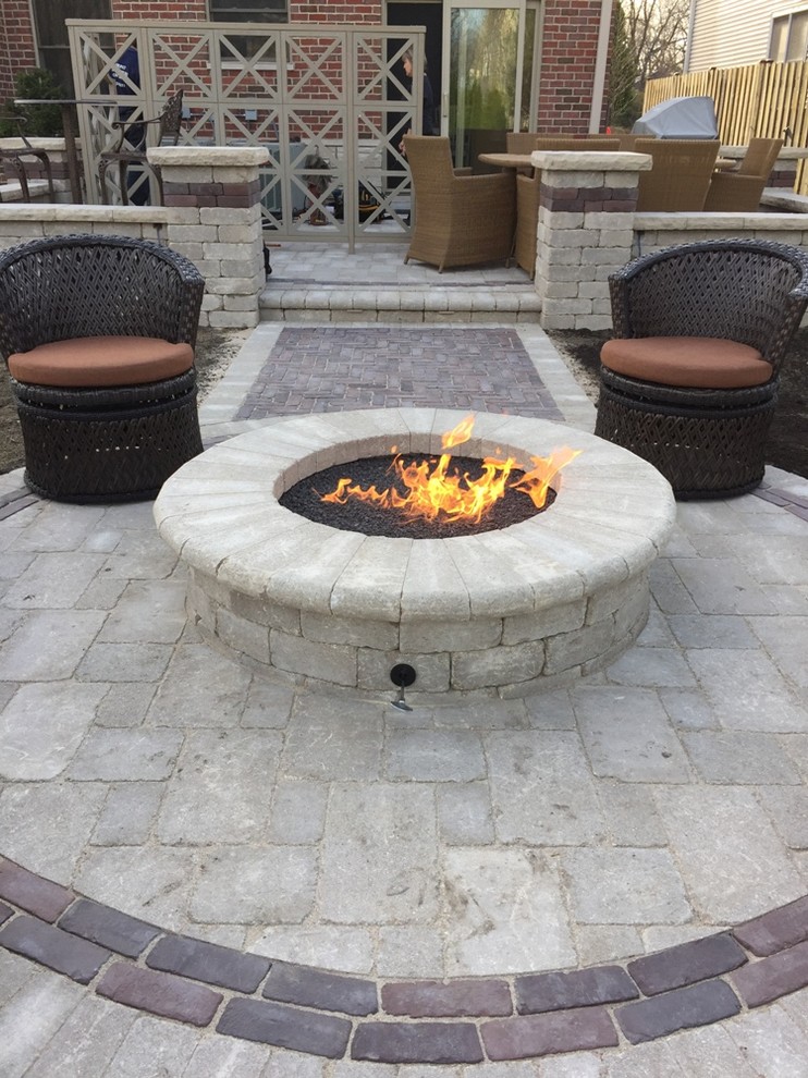 This is an example of a large traditional backyard patio in Chicago with a fire feature, natural stone pavers and no cover.