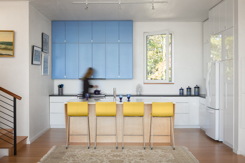 This is an example of a contemporary l-shaped kitchen in Portland Maine with flat-panel cabinets, blue cabinets, white appliances, with island and medium hardwood floors.