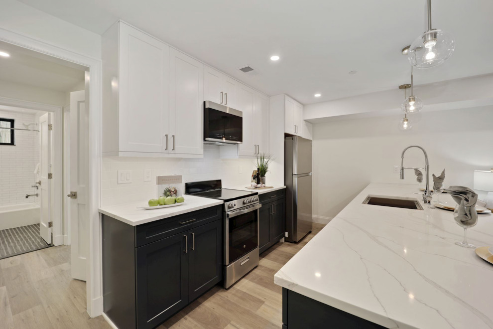 Contemporary galley kitchen in DC Metro with an undermount sink, shaker cabinets, white cabinets, stainless steel appliances, with island, brown floor and white benchtop.