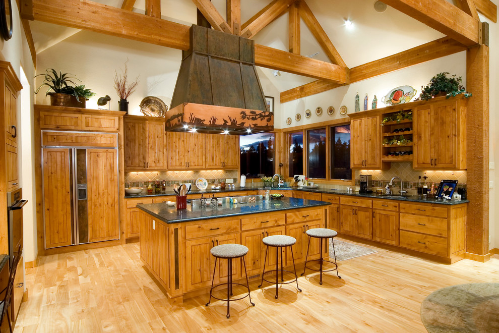 Photo of a country l-shaped open plan kitchen in Other with an undermount sink, recessed-panel cabinets, medium wood cabinets, stone tile splashback, panelled appliances, light hardwood floors, with island and beige floor.