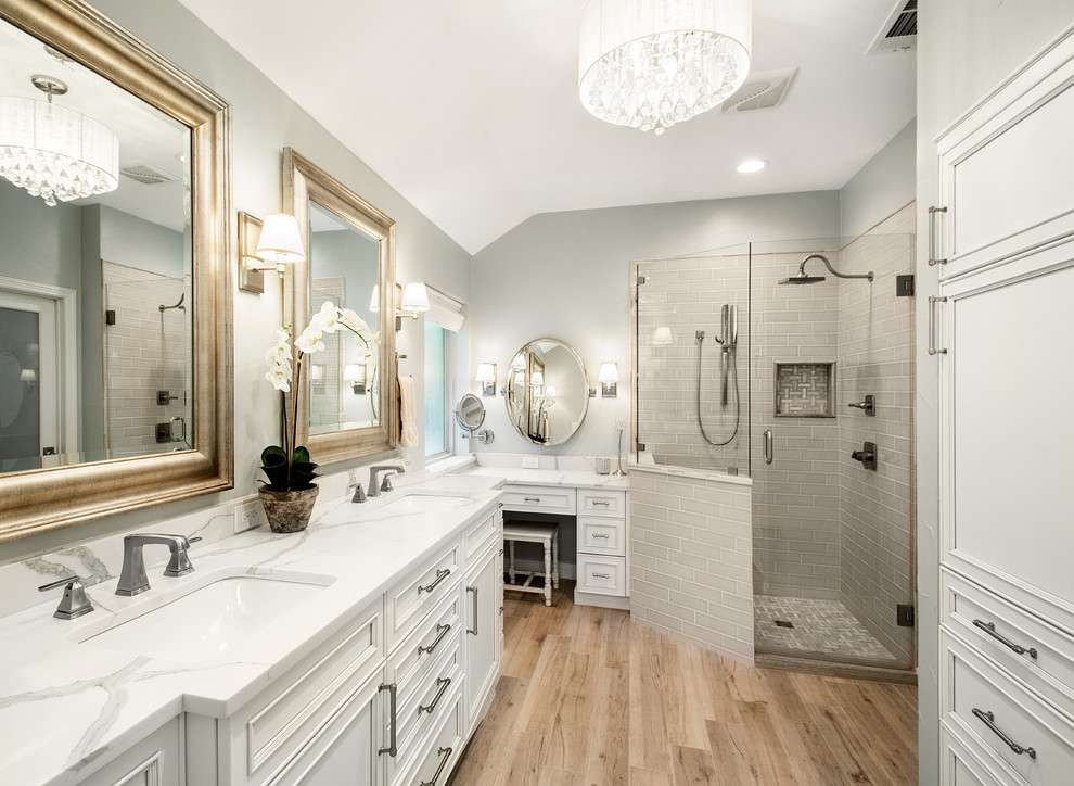 Inspiration for a mid-sized transitional master bathroom in Dallas with recessed-panel cabinets, white cabinets, a corner shower, gray tile, marble, grey walls, porcelain floors, an undermount sink, engineered quartz benchtops, brown floor, a hinged shower door and white benchtops.