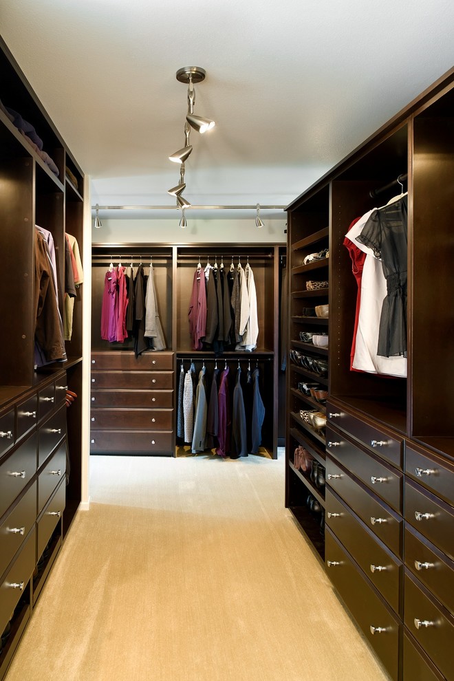 This is an example of a large traditional gender-neutral walk-in wardrobe in Portland with raised-panel cabinets, dark wood cabinets and carpet.
