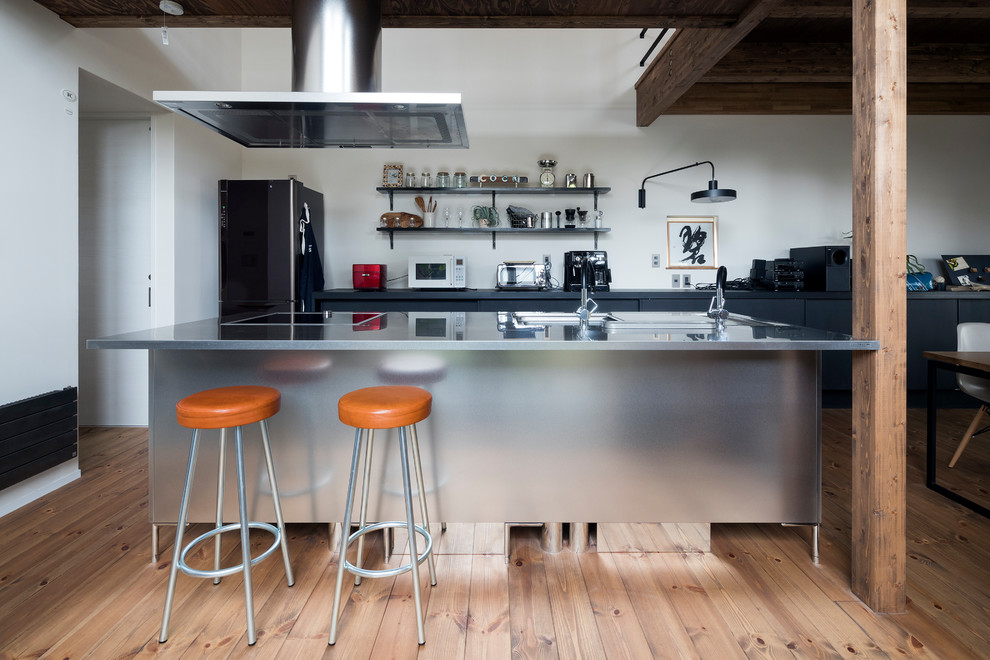 Industrial galley open plan kitchen in Other with a single-bowl sink, flat-panel cabinets, black cabinets, stainless steel benchtops, light hardwood floors, with island and brown floor.