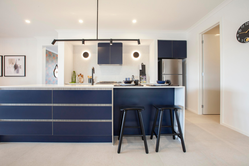 Design ideas for a single-wall open plan kitchen in Melbourne with blue cabinets, quartz benchtops, white splashback, ceramic splashback, stainless steel appliances, ceramic floors, with island, beige floor and white benchtop.