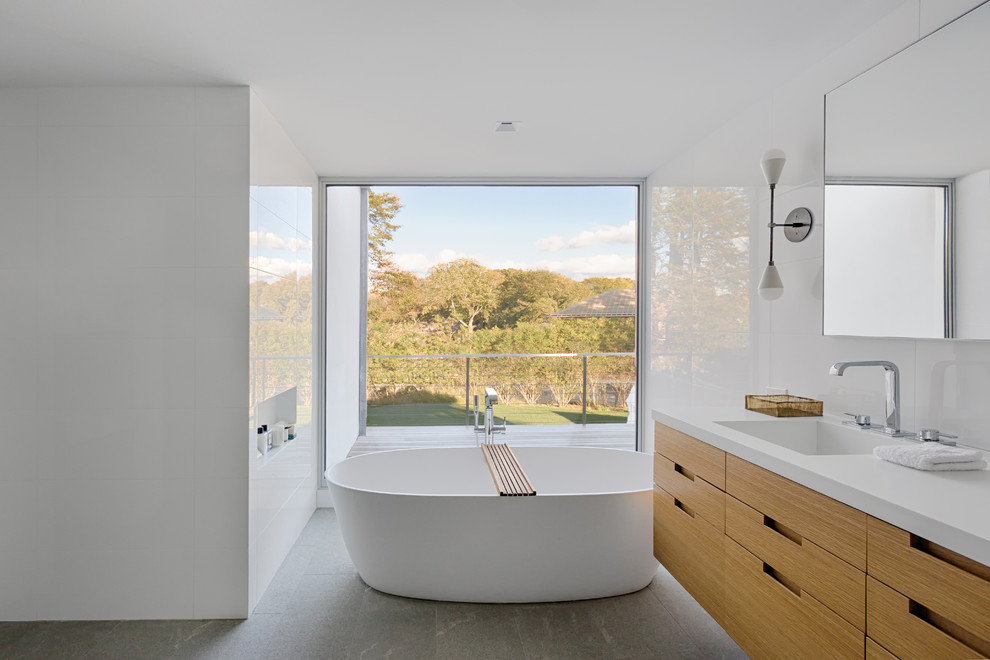 Inspiration for a large modern master white tile and porcelain tile gray floor freestanding bathtub remodel in New York with flat-panel cabinets, medium tone wood cabinets, an integrated sink, quartz countertops and white walls
