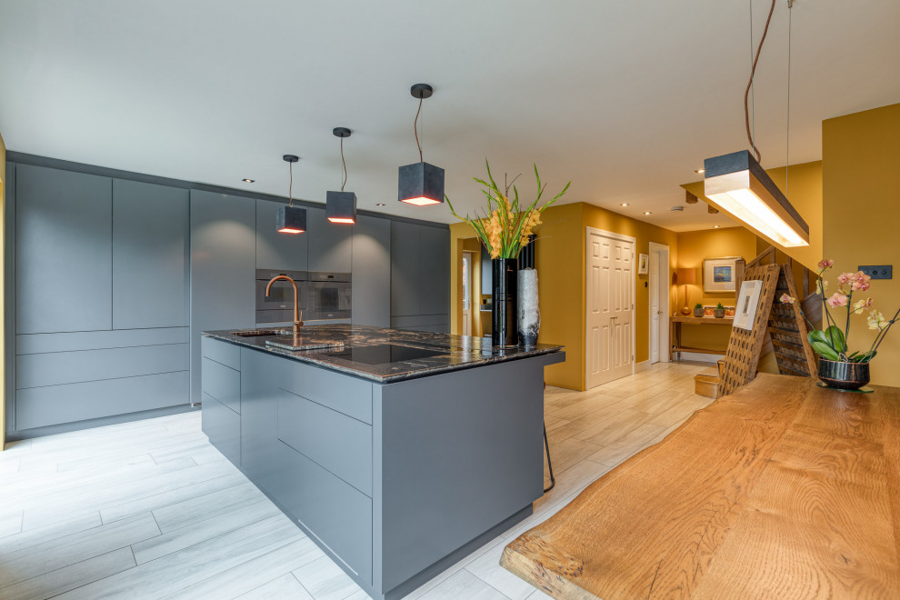 Photo of a large contemporary l-shaped open plan kitchen in Hertfordshire with a drop-in sink, louvered cabinets, grey cabinets, granite benchtops, panelled appliances, with island and black benchtop.