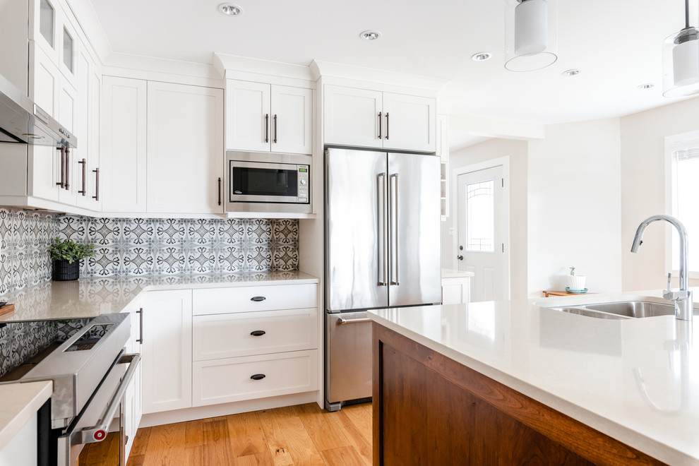 Inspiration for a mid-sized transitional l-shaped medium tone wood floor and brown floor kitchen pantry remodel with an undermount sink, shaker cabinets, white cabinets, quartzite countertops, gray backsplash, porcelain backsplash, stainless steel appliances, an island and white countertops