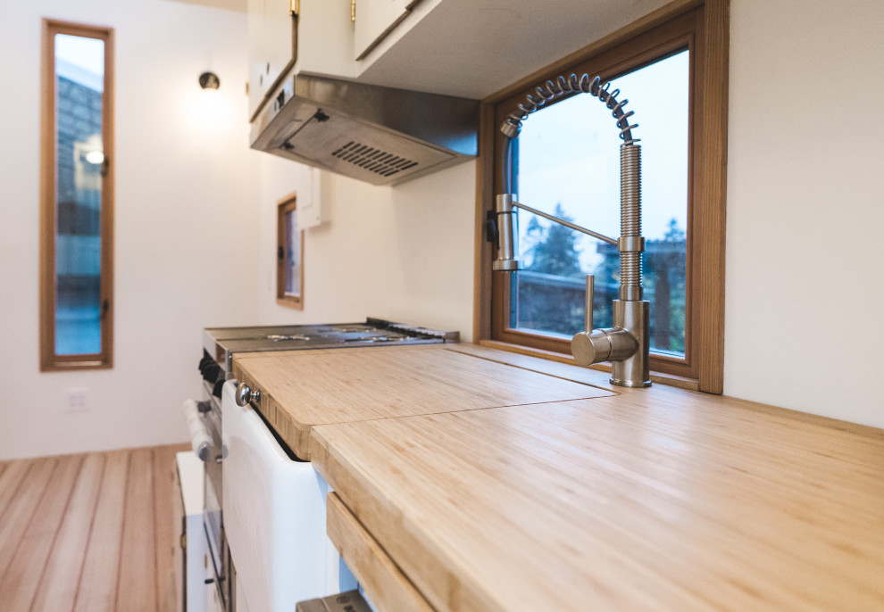 Idéer för ett litet modernt brun linjärt kök, med en rustik diskho, släta luckor, vita skåp, träbänkskiva, vitt stänkskydd, stänkskydd i trä, rostfria vitvaror, mellanmörkt trägolv och rött golv