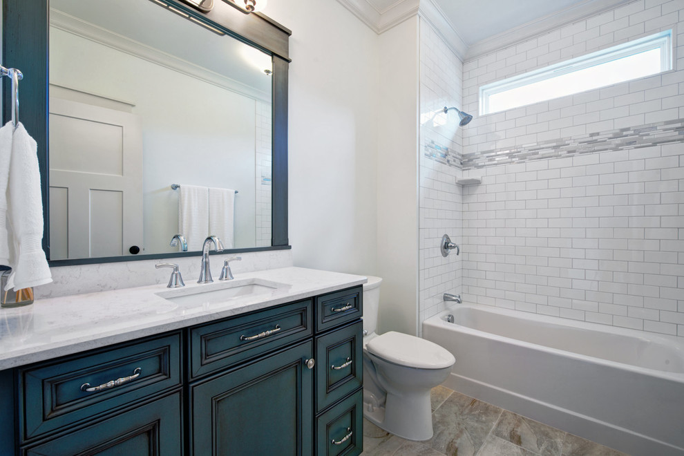 This is an example of a mid-sized arts and crafts 3/4 bathroom in Other with furniture-like cabinets, blue cabinets, an alcove tub, a shower/bathtub combo, a two-piece toilet, gray tile, white tile, subway tile, white walls, ceramic floors, an undermount sink and engineered quartz benchtops.