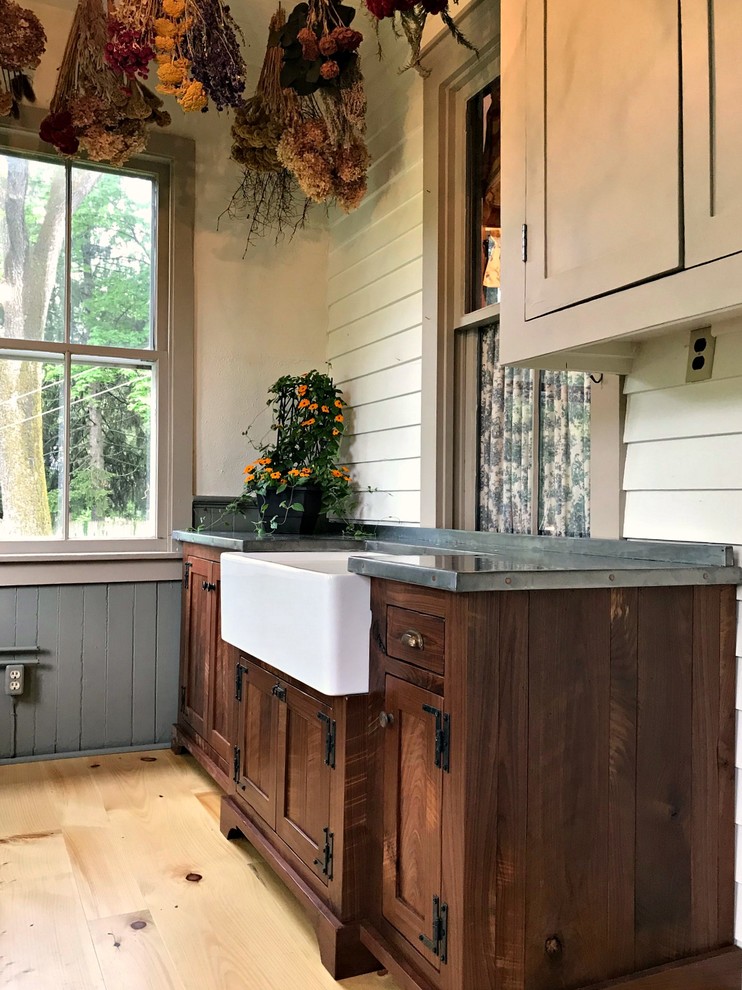 Design ideas for a mid-sized country utility room in Philadelphia with a farmhouse sink, shaker cabinets, dark wood cabinets, zinc benchtops, beige walls, light hardwood floors, brown floor and grey benchtop.