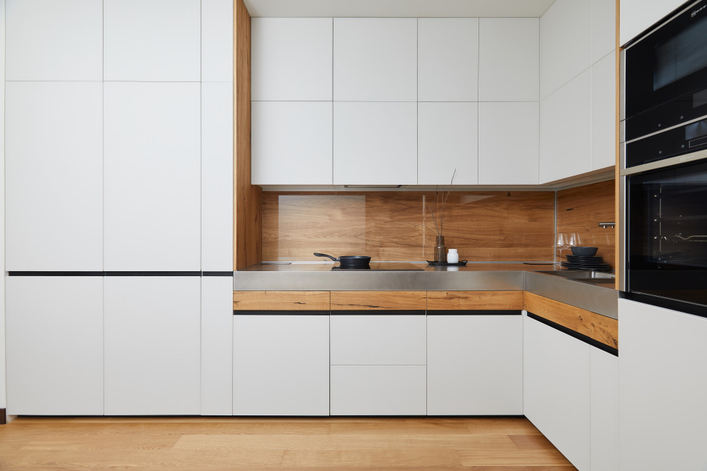 Mid-sized contemporary l-shaped eat-in kitchen in Moscow with a double-bowl sink, white cabinets, stainless steel benchtops, brown splashback, timber splashback, panelled appliances, no island, grey benchtop, flat-panel cabinets, medium hardwood floors and brown floor.