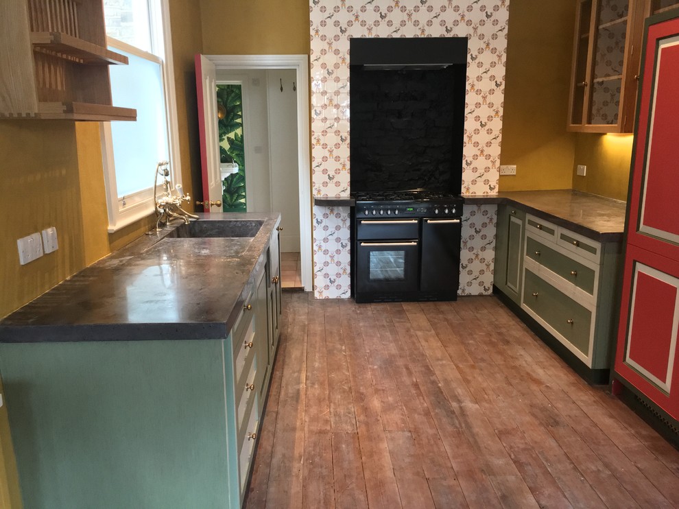 This is an example of a mid-sized traditional open plan kitchen in London with an integrated sink, beaded inset cabinets, green cabinets, concrete benchtops, yellow splashback, panelled appliances and painted wood floors.