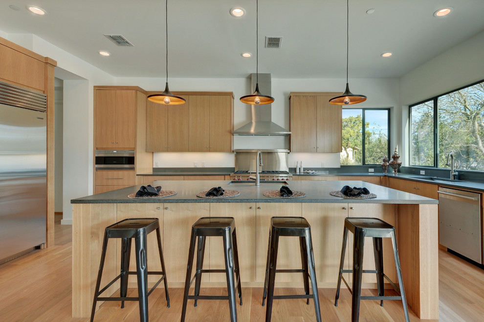Inspiration for a contemporary l-shaped kitchen in Austin with an undermount sink, flat-panel cabinets, light wood cabinets, stainless steel appliances, light hardwood floors and with island.