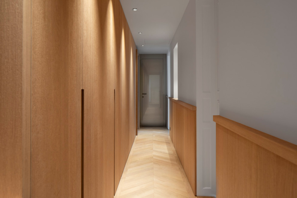 Cette image montre un grand couloir traditionnel en bois avec un mur blanc, parquet clair et un sol beige.