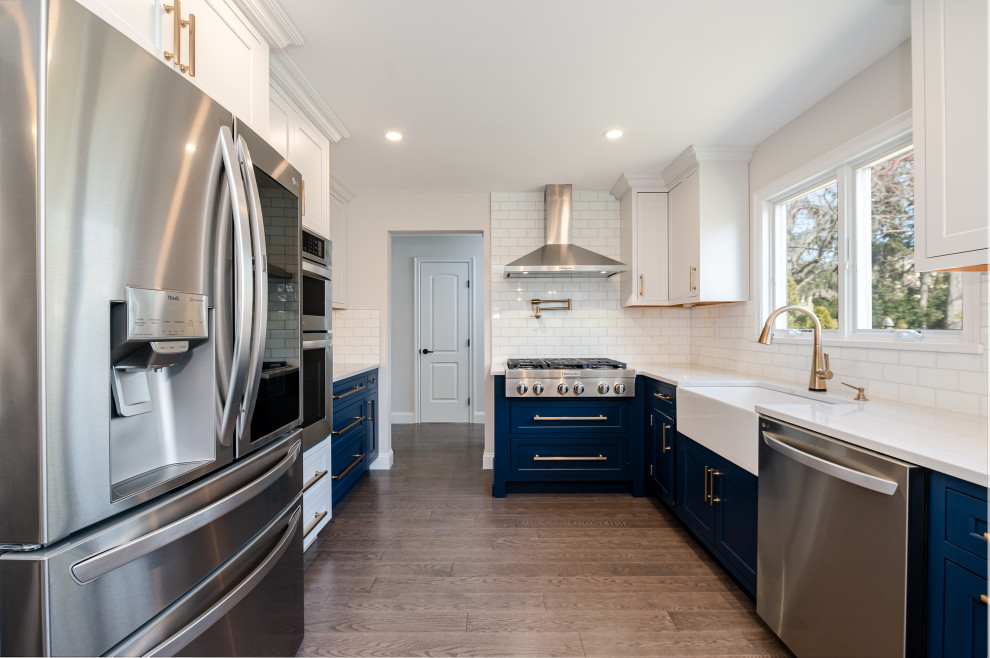 Inspiration for a mid-sized contemporary u-shaped eat-in kitchen in New York with a farmhouse sink, beaded inset cabinets, blue cabinets, quartz benchtops, white splashback, ceramic splashback, stainless steel appliances, light hardwood floors, a peninsula, brown floor and white benchtop.