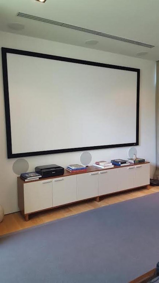 This is an example of a mid-sized contemporary enclosed home theatre with white walls, light hardwood floors, a projector screen and beige floor.