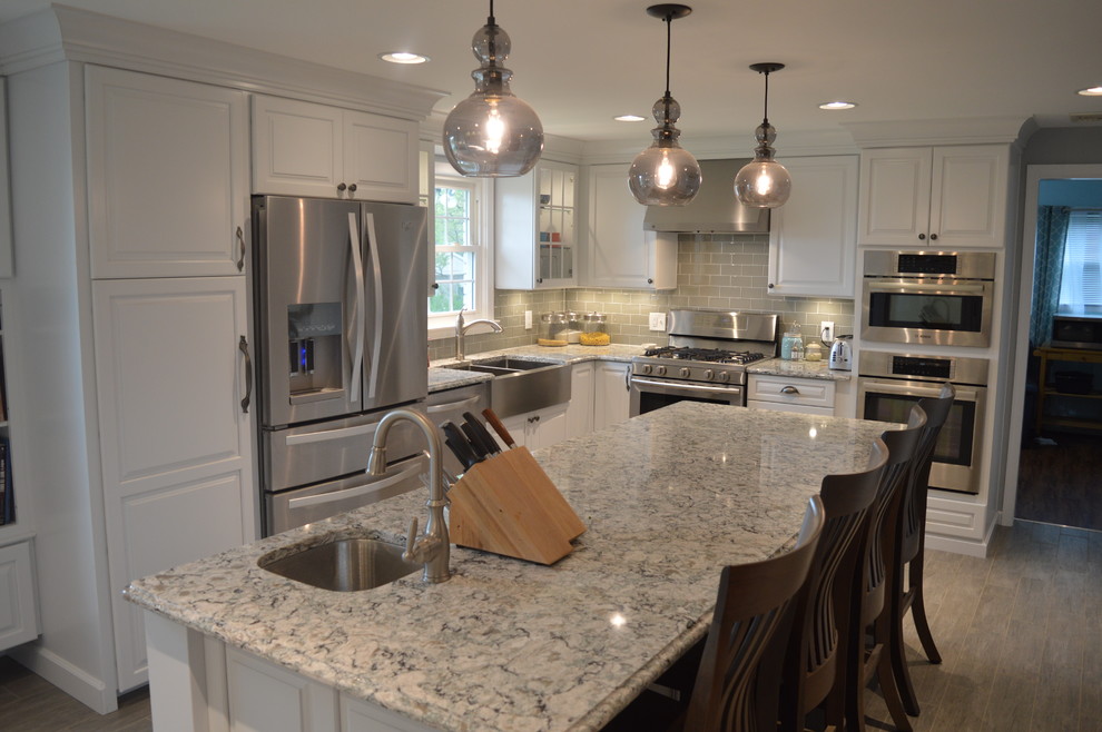 Enclosed kitchen - large transitional u-shaped ceramic tile and gray floor enclosed kitchen idea with a farmhouse sink, raised-panel cabinets, white cabinets, quartz countertops, gray backsplash, glass tile backsplash, stainless steel appliances and an island