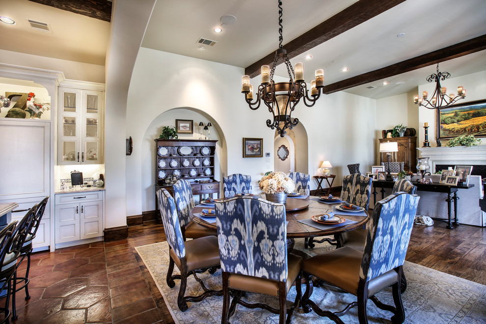 This is an example of a mid-sized mediterranean open plan dining in Dallas with a standard fireplace, a stone fireplace surround, dark hardwood floors, white walls and brown floor.