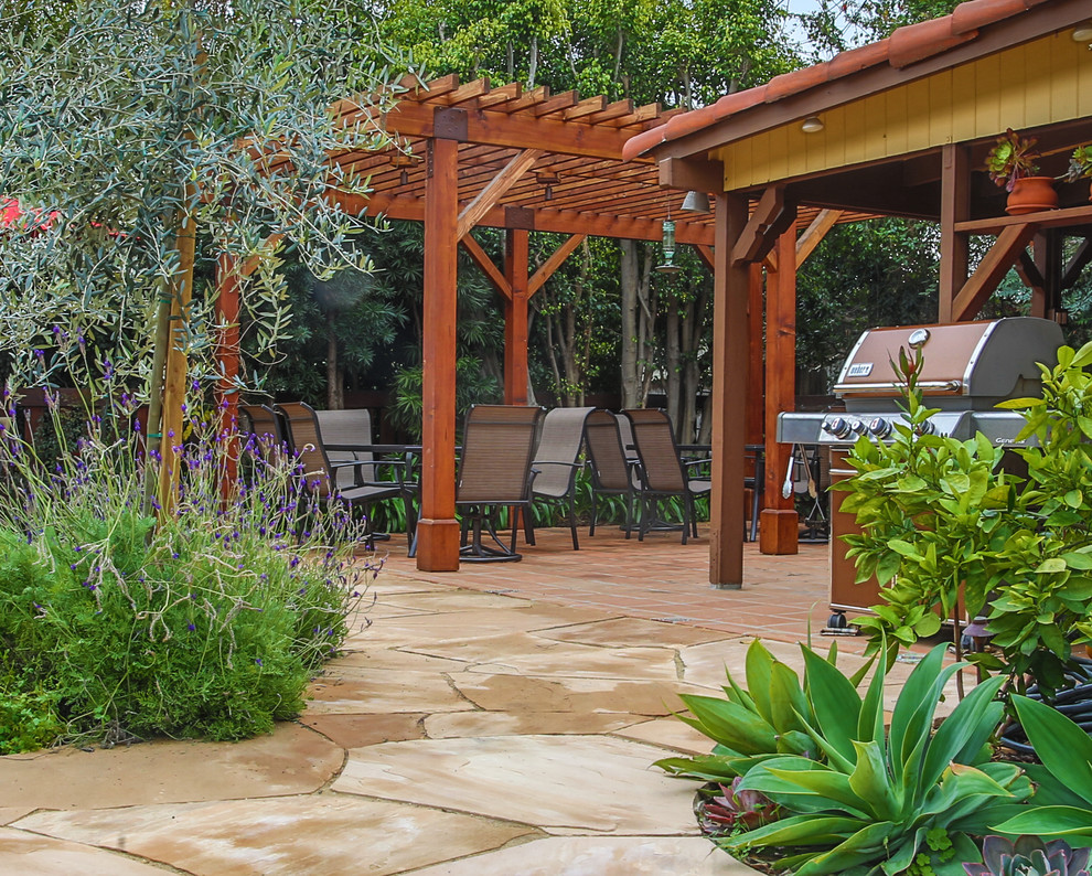Mittelgroßer Mediterraner Garten hinter dem Haus, im Frühling mit Pflastersteinen, Feuerstelle, direkter Sonneneinstrahlung und Holzzaun in Los Angeles