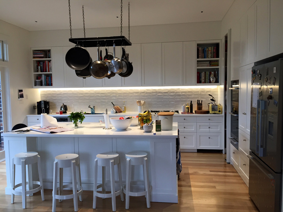 Photo of a mid-sized traditional galley eat-in kitchen in Sydney with a single-bowl sink, recessed-panel cabinets, white cabinets, quartz benchtops, white splashback, subway tile splashback, stainless steel appliances, medium hardwood floors and with island.