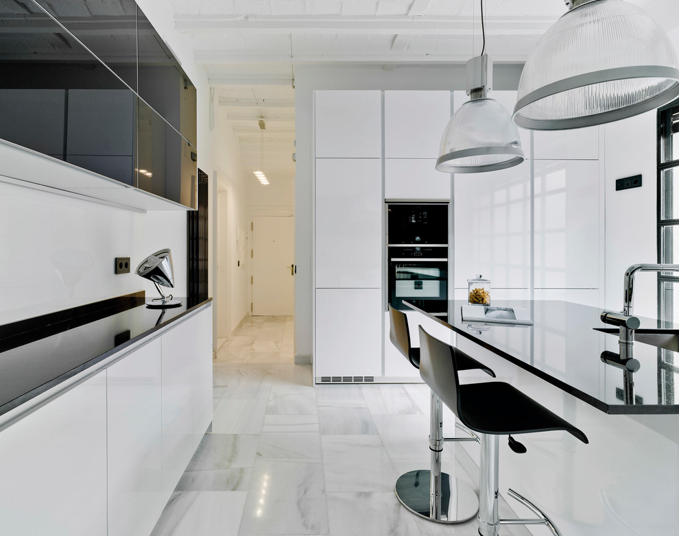 Inspiration for a contemporary kitchen in Madrid with an undermount sink, flat-panel cabinets, white cabinets, granite benchtops, white splashback, black appliances, with island, white floor and marble floors.