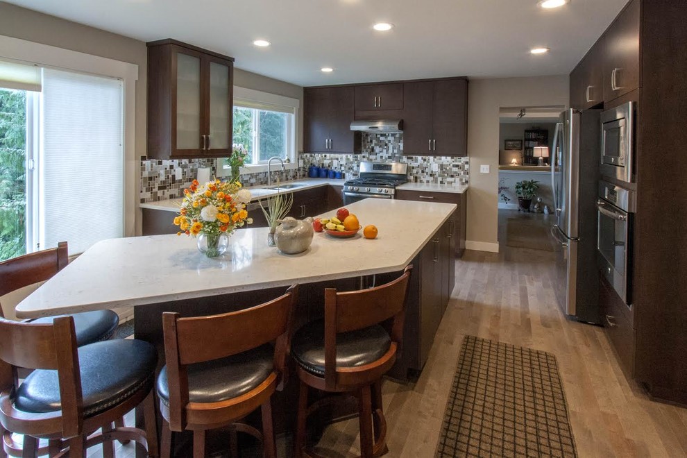 This is an example of a contemporary l-shaped eat-in kitchen in Seattle with an undermount sink, flat-panel cabinets, brown cabinets, quartz benchtops, grey splashback, glass tile splashback, stainless steel appliances, light hardwood floors, with island and beige floor.