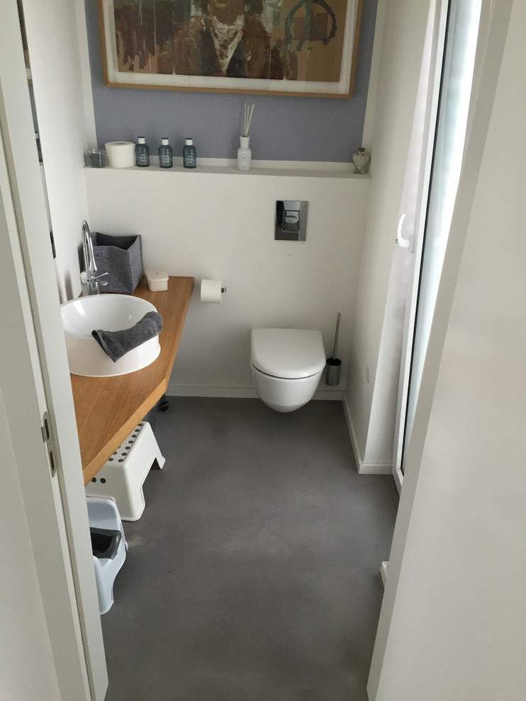 Design ideas for a small contemporary powder room in Cologne with a wall-mount toilet, white walls, a vessel sink, wood benchtops, grey floor, stone tile, concrete floors and brown benchtops.
