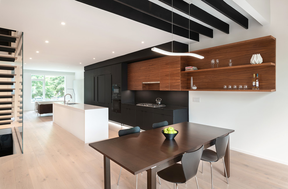 This is an example of a contemporary open plan kitchen in DC Metro with an undermount sink, flat-panel cabinets, black splashback, black appliances, light hardwood floors, with island, beige floor and black benchtop.