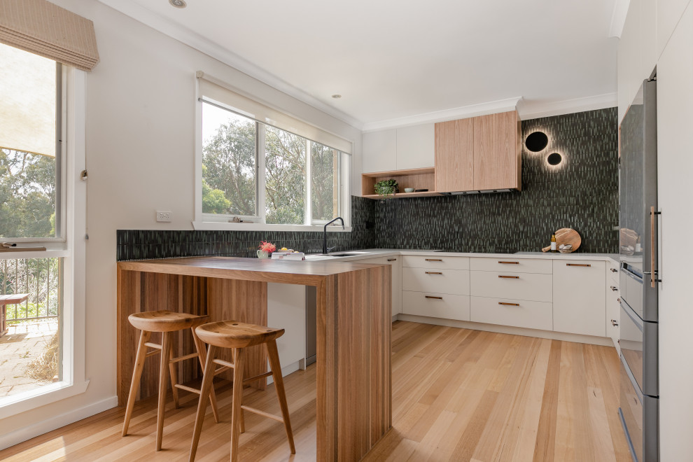 Inspiration for a contemporary u-shaped kitchen in Melbourne with an undermount sink, flat-panel cabinets, white cabinets, black splashback, panelled appliances, light hardwood floors, a peninsula, beige floor and white benchtop.