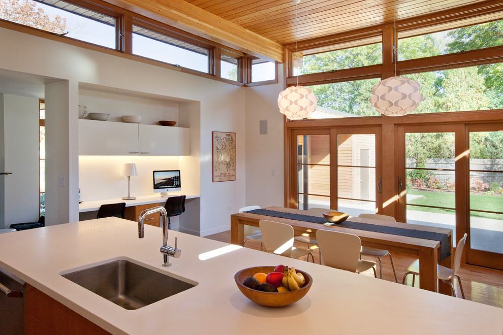 This is an example of a mid-sized modern single-wall eat-in kitchen in Boston with a single-bowl sink, solid surface benchtops, flat-panel cabinets, white cabinets, stainless steel appliances, dark hardwood floors, with island and brown floor.