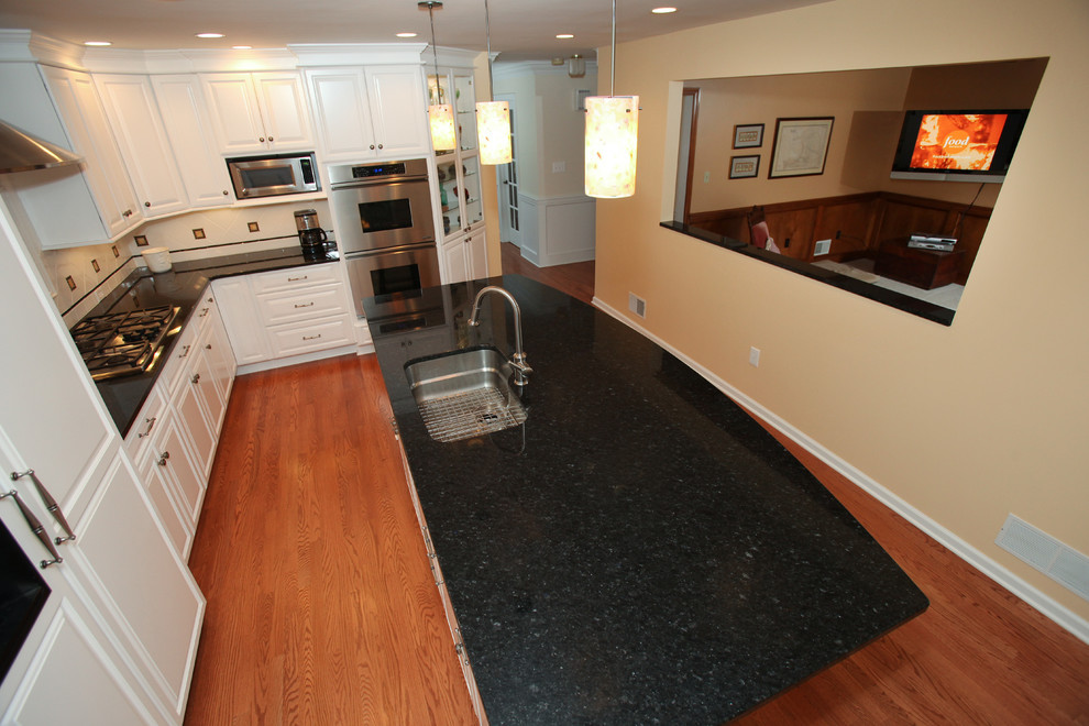 Inspiration for a mid-sized transitional l-shaped medium tone wood floor kitchen remodel with an undermount sink, raised-panel cabinets, white cabinets, quartz countertops, white backsplash, ceramic backsplash, stainless steel appliances and an island
