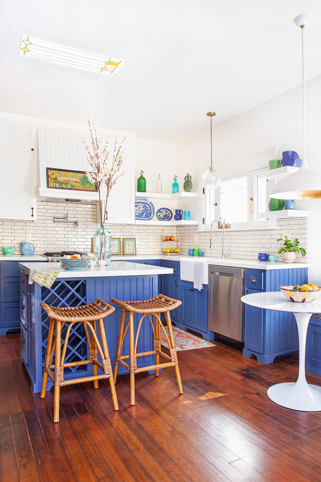 Enclosed kitchen - mid-sized craftsman l-shaped dark wood floor and brown floor enclosed kitchen idea in Los Angeles with a farmhouse sink, shaker cabinets, blue cabinets, quartz countertops, white backsplash, ceramic backsplash, stainless steel appliances, an island and white countertops