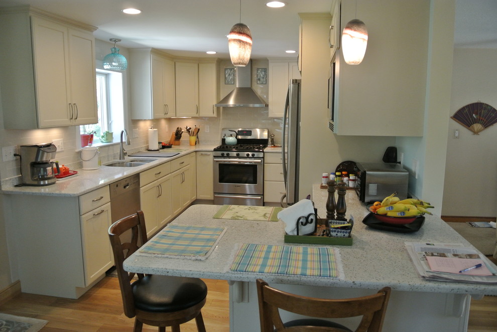 Inspiration for a transitional l-shaped medium tone wood floor eat-in kitchen remodel in Boston with an undermount sink, shaker cabinets, white cabinets, recycled glass countertops, white backsplash, subway tile backsplash, stainless steel appliances, a peninsula and white countertops