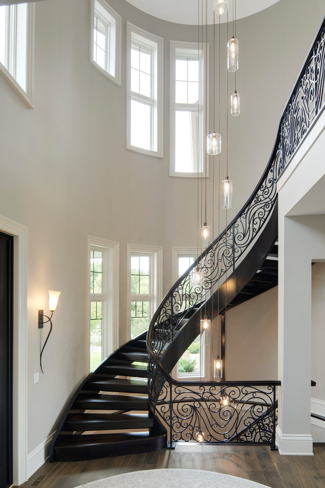 Expansive traditional wood curved staircase in Minneapolis with open risers and metal railing.