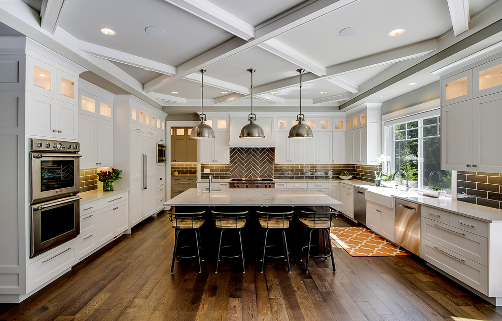 This is an example of a large traditional kitchen in Seattle with a farmhouse sink, shaker cabinets, white cabinets, quartz benchtops, stainless steel appliances, dark hardwood floors, with island, brown floor, black splashback and subway tile splashback.
