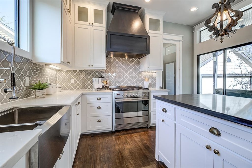 This is an example of a mid-sized arts and crafts l-shaped open plan kitchen in Houston with a farmhouse sink, shaker cabinets, white cabinets, concrete benchtops, grey splashback, ceramic splashback, stainless steel appliances, dark hardwood floors, with island, brown floor and grey benchtop.