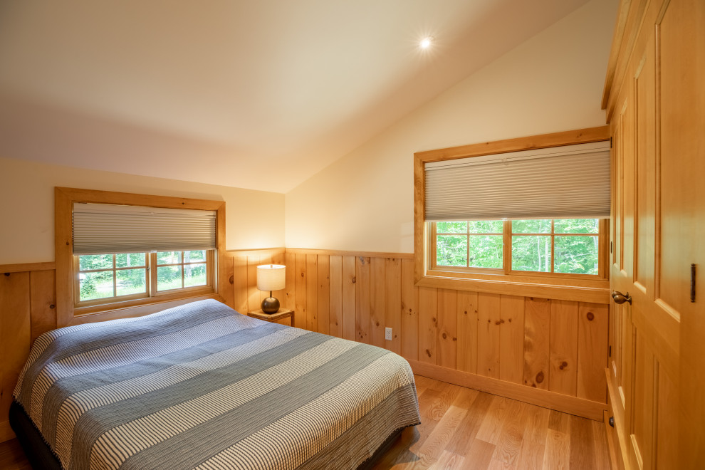 This is an example of a mid-sized country guest bedroom in Portland Maine with light hardwood floors, beige floor, beige walls, no fireplace and decorative wall panelling.