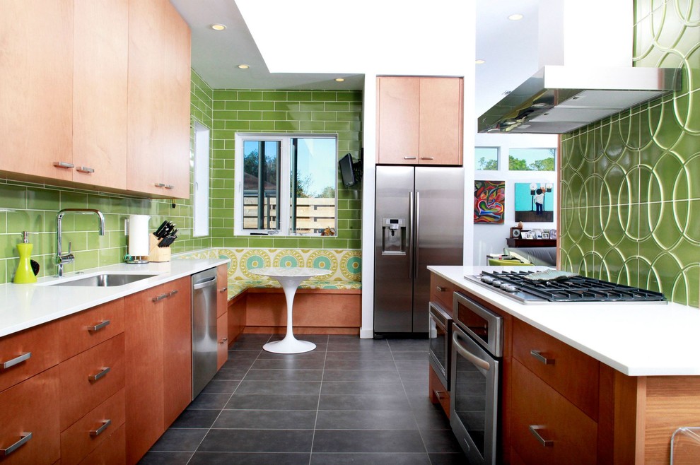 Modern galley eat-in kitchen in New Orleans with an undermount sink, flat-panel cabinets, medium wood cabinets, green splashback, subway tile splashback, stainless steel appliances and grey floor.