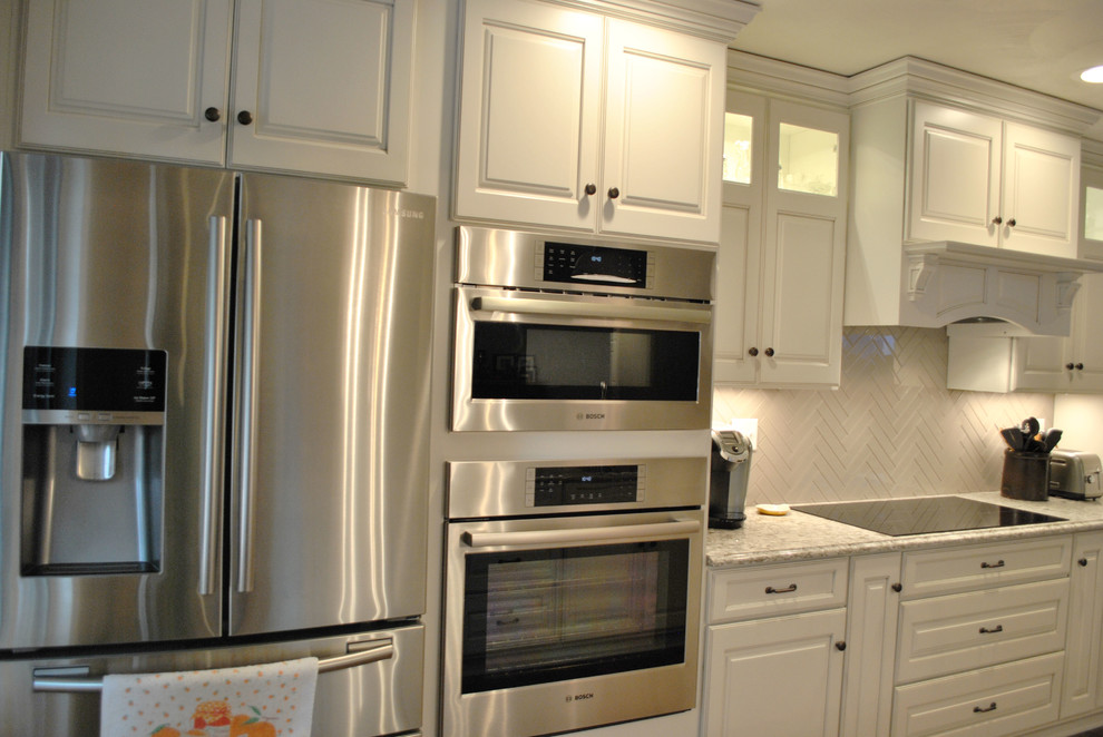 Example of a transitional l-shaped medium tone wood floor open concept kitchen design in St Louis with raised-panel cabinets, white cabinets, granite countertops, white backsplash, ceramic backsplash, stainless steel appliances and an island