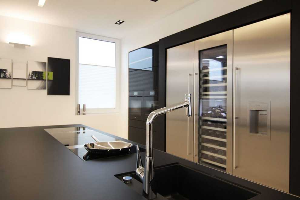 This is an example of an expansive contemporary galley open plan kitchen in Other with an integrated sink, flat-panel cabinets, stainless steel cabinets, solid surface benchtops, stainless steel appliances, with island and black benchtop.