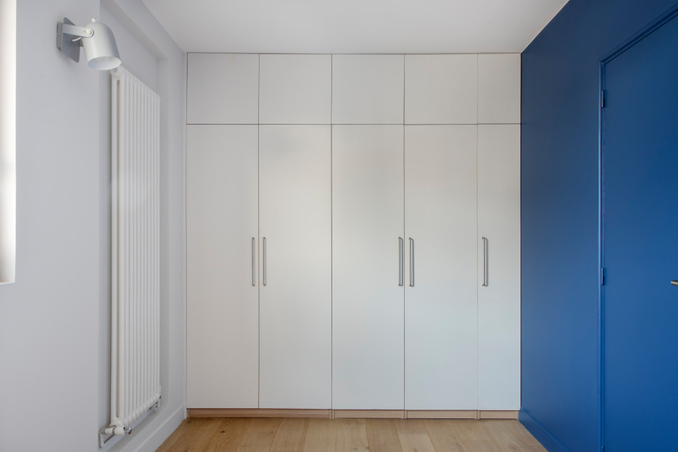 Idee per uno spazio per vestirsi unisex minimalista di medie dimensioni con ante a filo, ante bianche, parquet chiaro e pavimento beige