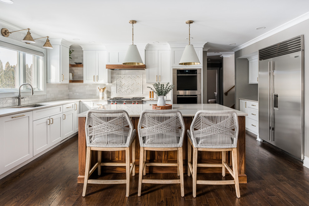 Example of a transitional u-shaped dark wood floor and brown floor kitchen design in Chicago with an undermount sink, shaker cabinets, white cabinets, gray backsplash, stainless steel appliances, an island and gray countertops