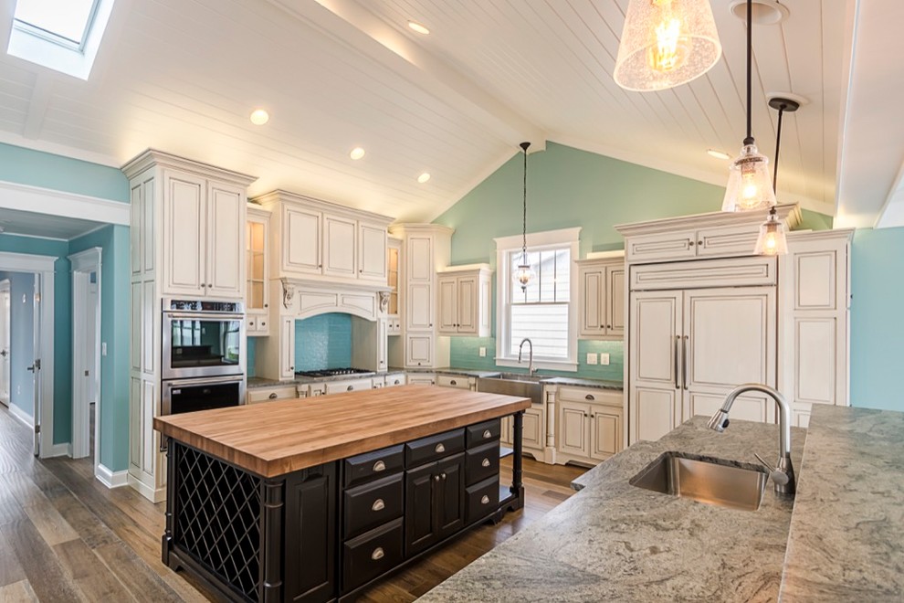 Inspiration for a large transitional u-shaped dark wood floor and brown floor kitchen remodel with a farmhouse sink, paneled appliances, blue backsplash, glass tile backsplash, gray countertops, raised-panel cabinets, beige cabinets and an island