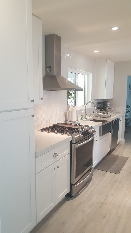 Enclosed kitchen - large transitional single-wall light wood floor and beige floor enclosed kitchen idea in Miami with a farmhouse sink, shaker cabinets, white cabinets, solid surface countertops, white backsplash, wood backsplash, stainless steel appliances and an island