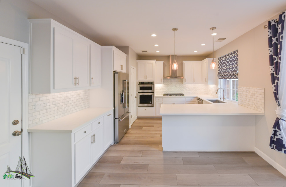 Photo of a mid-sized contemporary galley eat-in kitchen in Austin with an integrated sink, flat-panel cabinets, white cabinets, marble benchtops, white splashback, subway tile splashback, stainless steel appliances, light hardwood floors, a peninsula, brown floor and white benchtop.